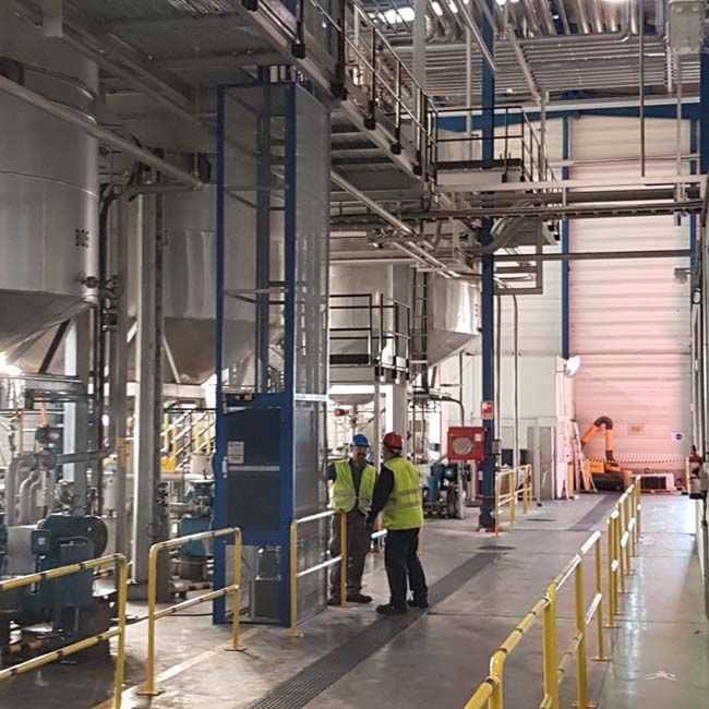 Un hombre con un chaleco amarillo está parado en una fábrica.