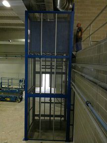 Un hombre está parado en la parte superior de un ascensor azul en un edificio.