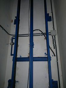 Un ascensor azul está en una habitación al lado de una pared blanca.