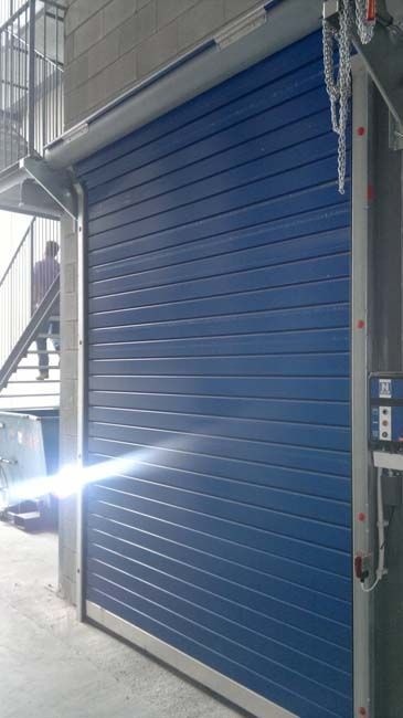 Una puerta enrollable azul en un edificio con escaleras al fondo.