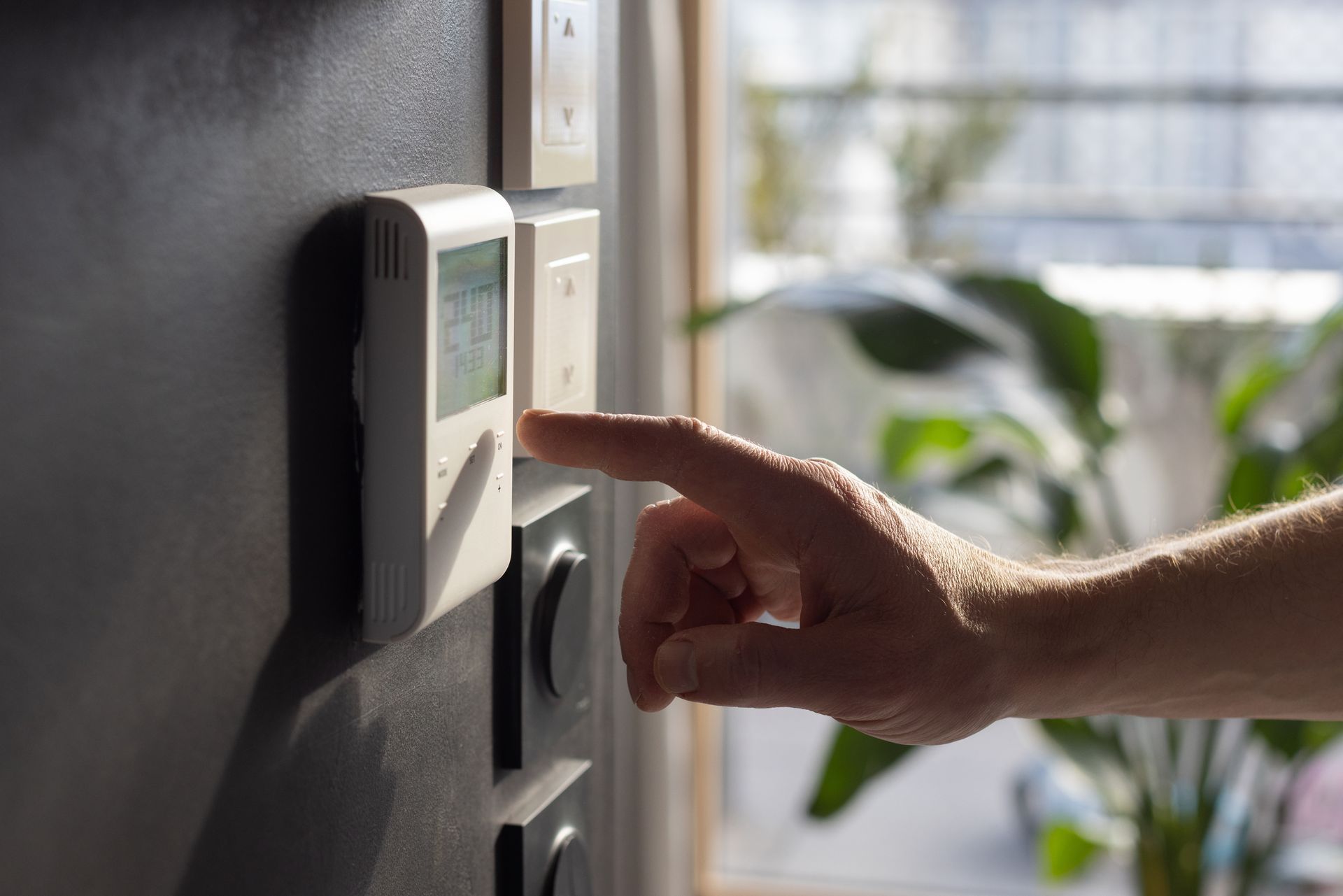 Main appuyant sur un thermostat mural dans un intérieur de maison baigné de soleil
