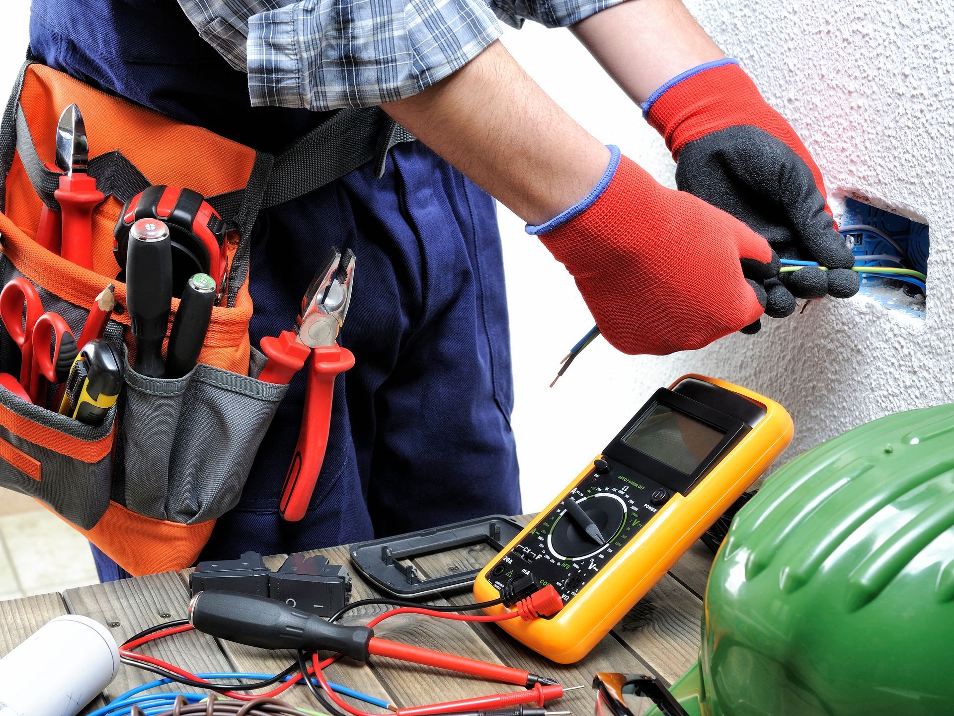 Électricien portant des gants rouges utilisant des outils et un multimètre sur le câblage d'un établi