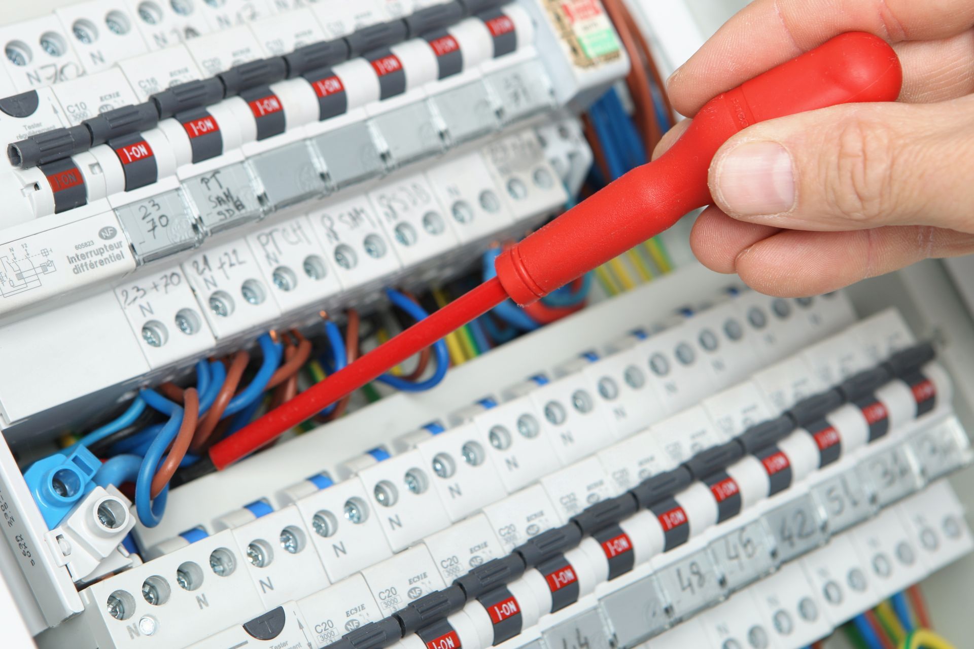 Main utilisant un tournevis rouge pour serrer les fils d'un tableau électrique