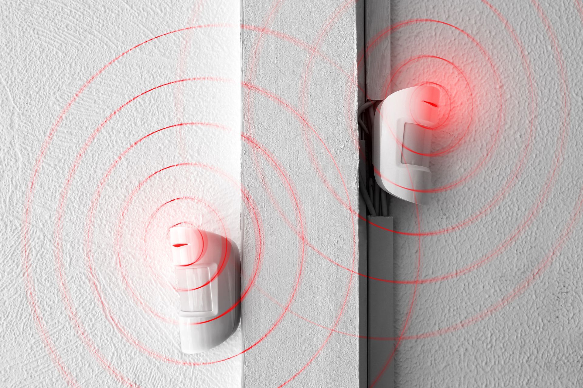 Deux capteurs blancs fixés au mur émettent des anneaux de signal sans fil rouges l'un vers l'autre.