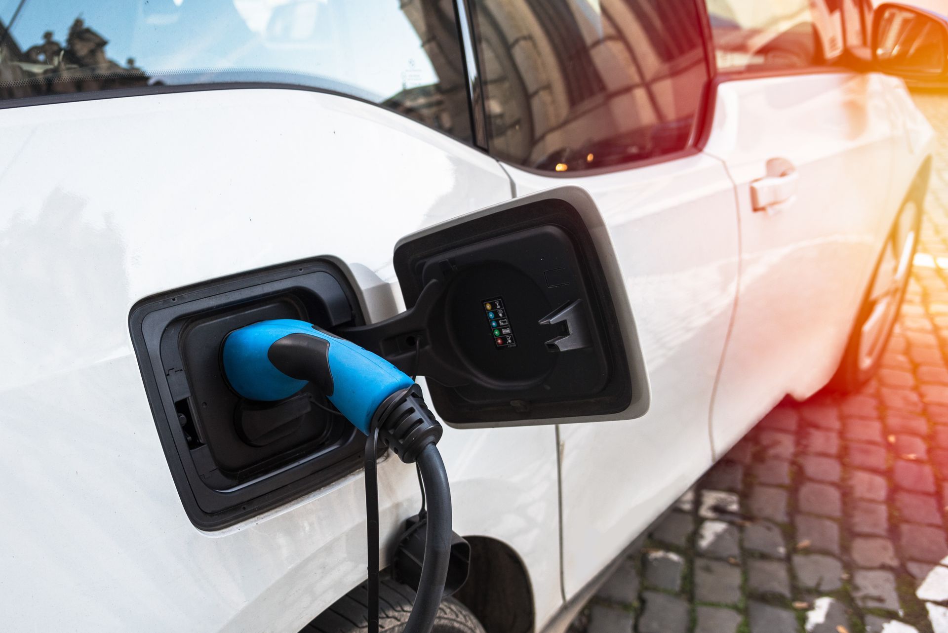 Recharge de voiture électrique avec prise bleue connectée à un véhicule blanc à l'extérieur