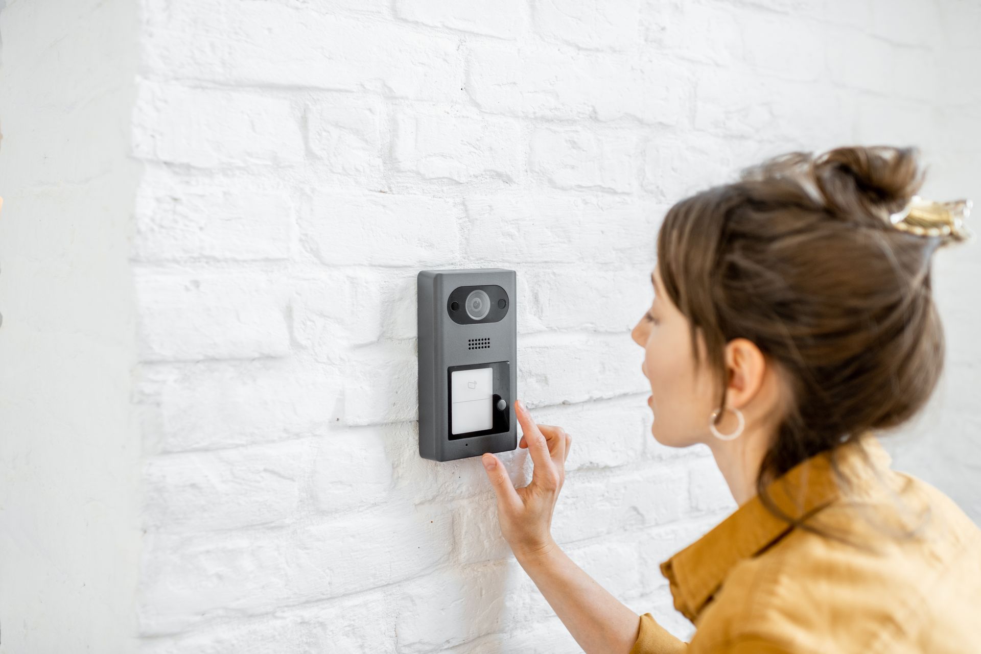 Une personne utilise une sonnette vidéo fixée sur un mur de briques blanches.