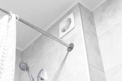 Douche blanche avec murs carrelés, tringle à rideau chromée et aération près du plafond