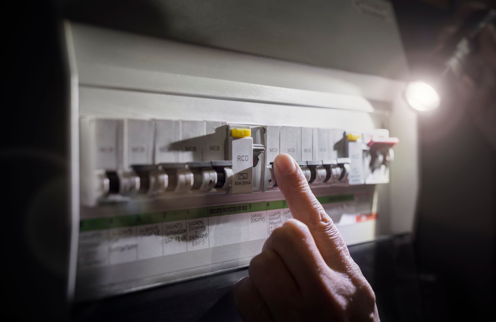 Un doigt pointant vers un tableau électrique éclairé dans une pièce faiblement éclairée
