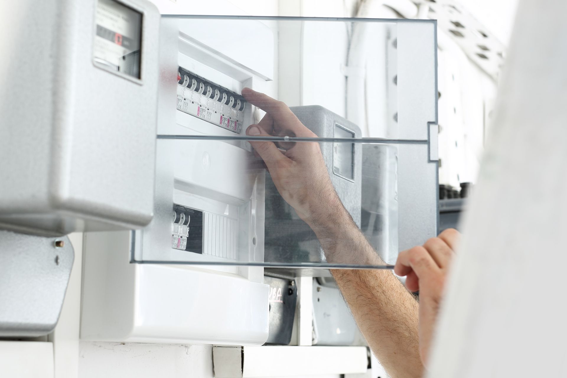 Des mains règlent les disjoncteurs d'un tableau électrique avec un compteur numérique