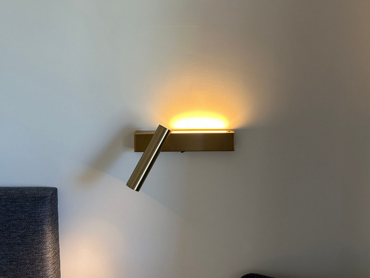 Applique murale moderne diffusant une lumière chaude sur un mur gris au-dessus du bord d'un meuble foncé