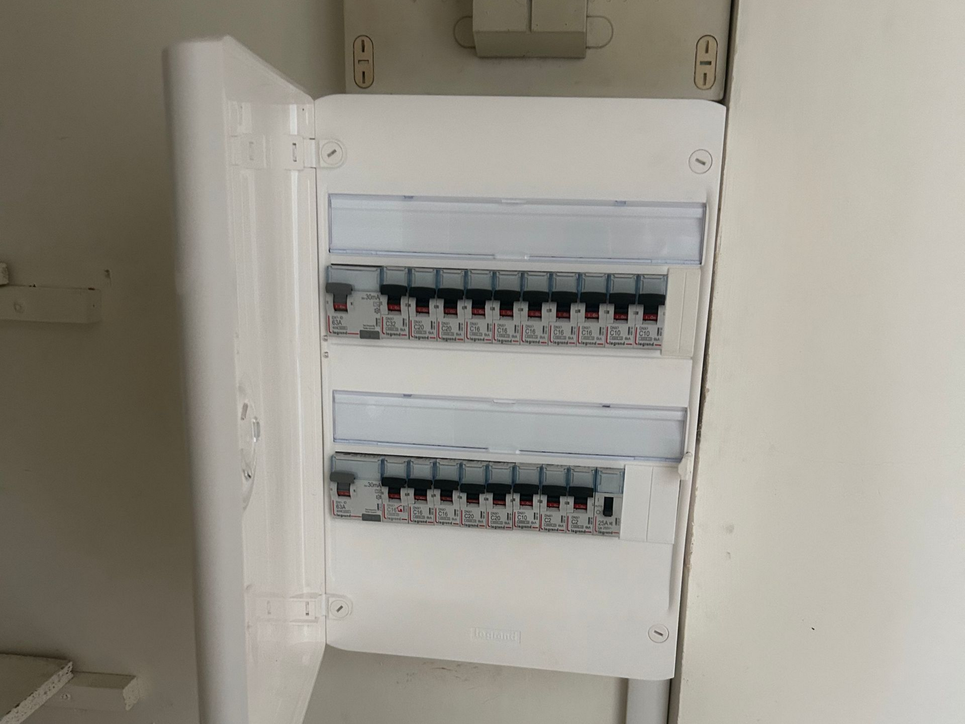 Tableau électrique ouvert avec deux rangées d'interrupteurs dans une armoire murale blanche