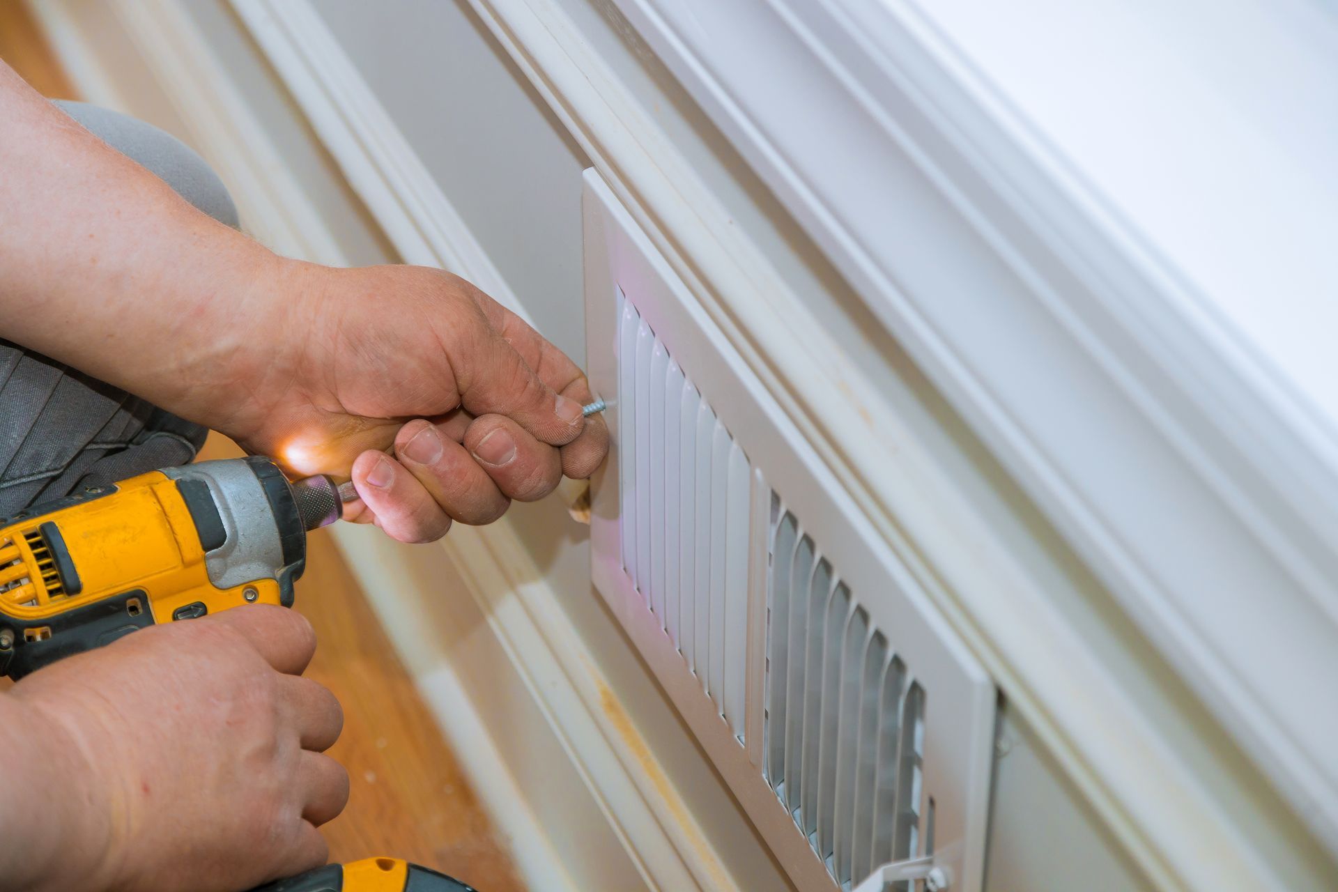 Des mains utilisent une perceuse jaune pour installer un cache-radiateur blanc sur un mur.