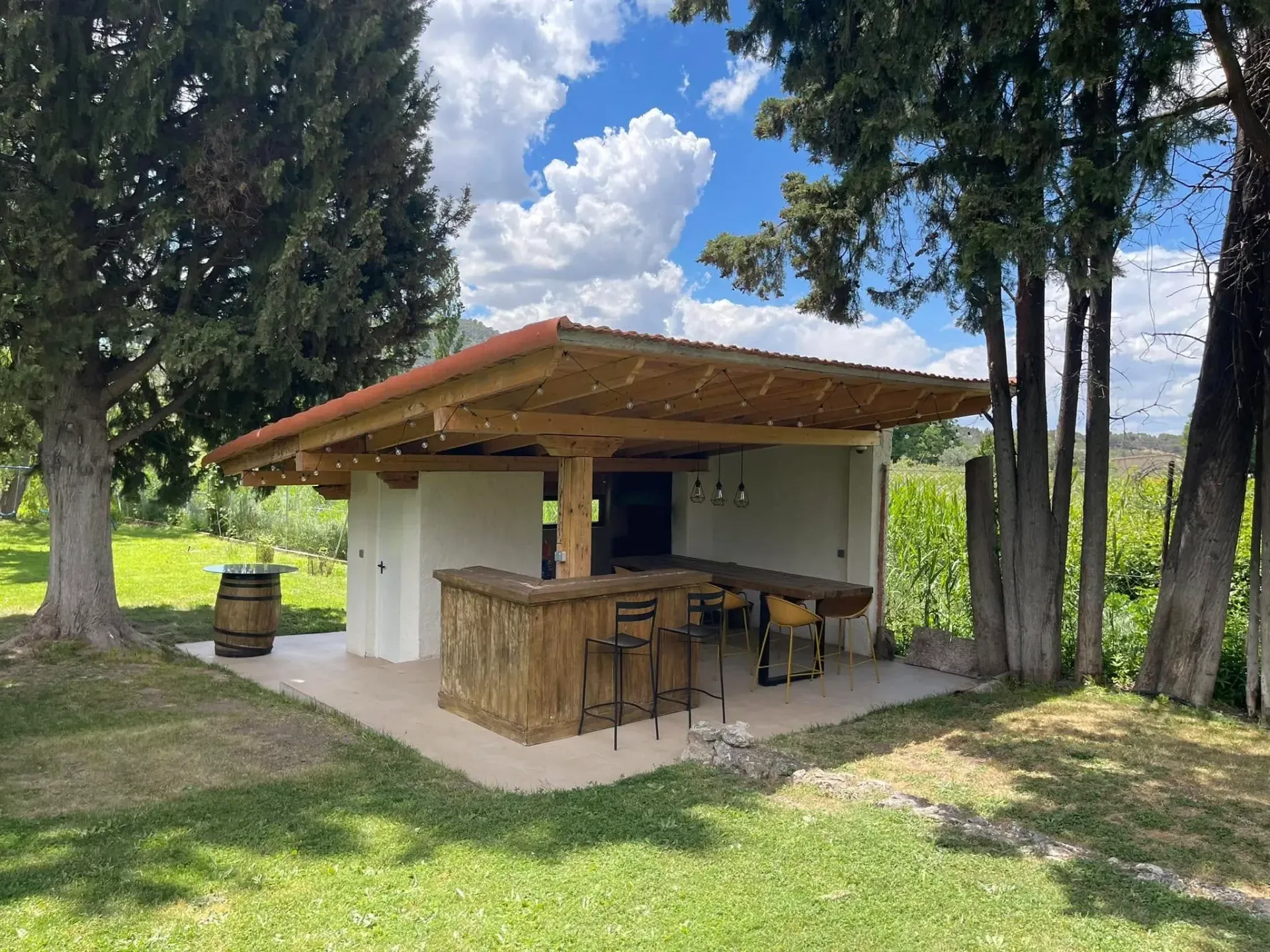 Un pequeño edificio con una barra de madera y taburetes en medio de un campo de hierba.
