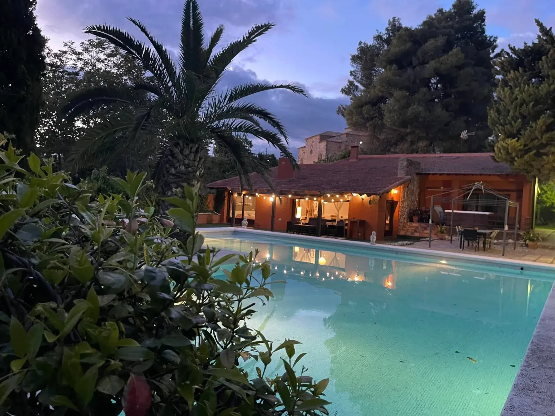 Una gran piscina está iluminada por la noche frente a una casa.