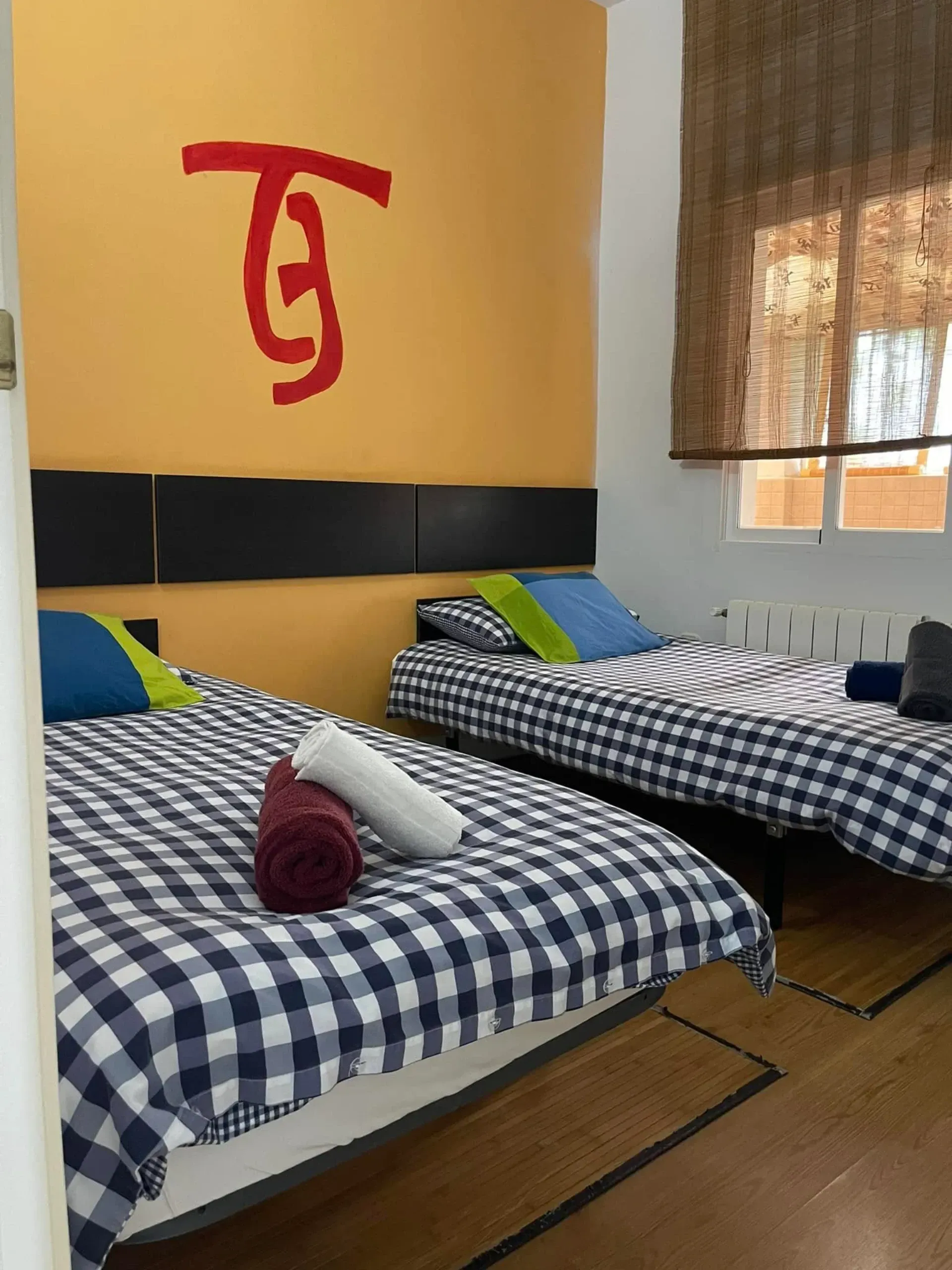 Un dormitorio con dos camas y una letra g roja en la pared.