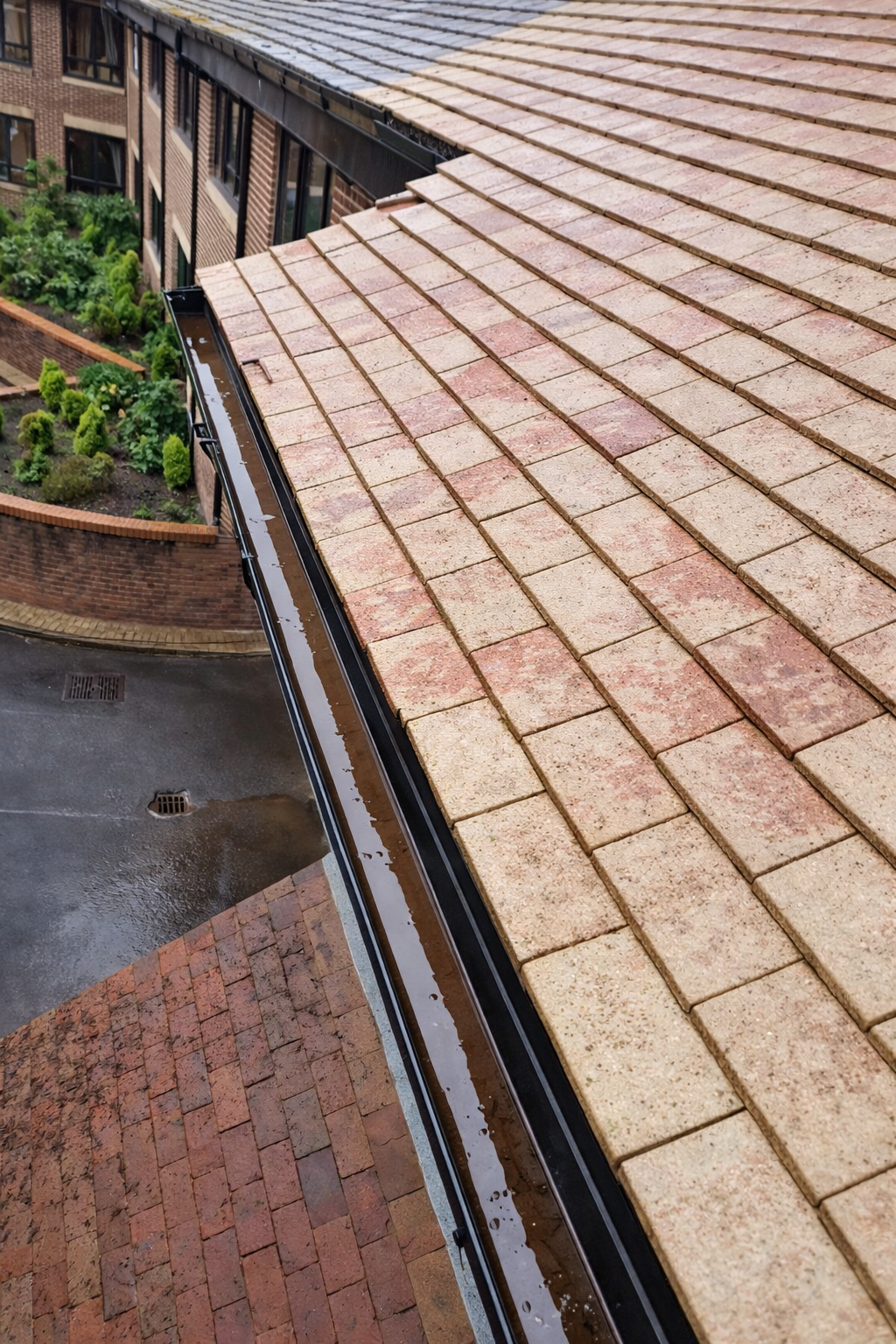 Curved tan roof with wet tiles beside a brick building and driveway below