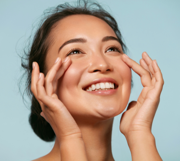 Femme souriante, se touchant les yeux, regardant vers le haut avec les mains près du visage ; peau claire, fond bleu.