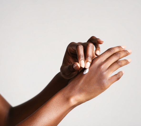 Personne appliquant de la crème sur ses mains. Peau foncée, fond clair.
