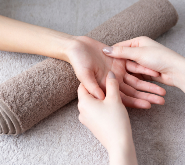 Mains massées sur une serviette roulée. Éclairage tamisé.