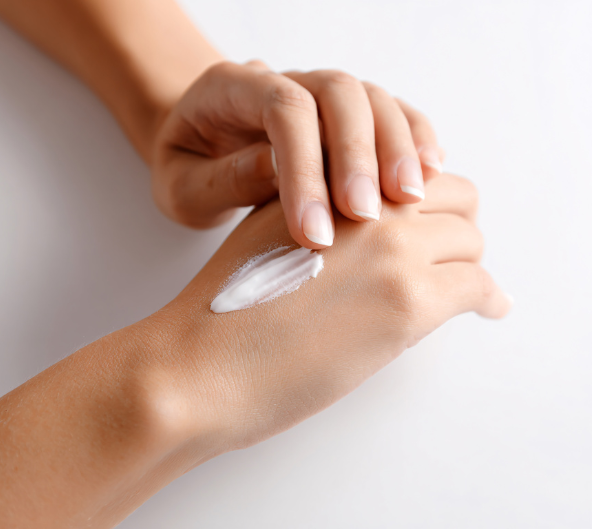 Personne appliquant de la crème blanche sur sa main sur une surface blanche.