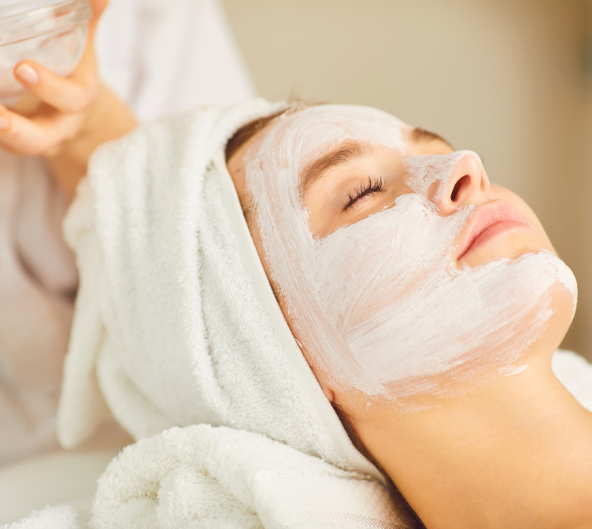 Femme avec un masque facial, les yeux fermés, enveloppée dans une serviette, recevant un soin spa.