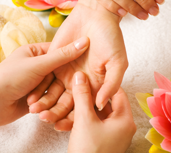 Mains recevant un massage, fleurs roses en arrière-plan.