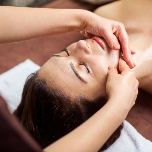 Personne recevant un massage facial ; mains sur le visage, yeux fermés, reposant sur une serviette.