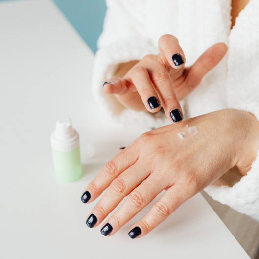 Des mains appliquant de la crème provenant d'un petit flacon vert sur une surface blanche.