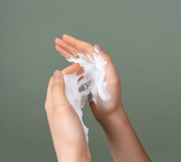 Des mains en coupe avec du savon blanc et mousseux sur un fond vert pâle.
