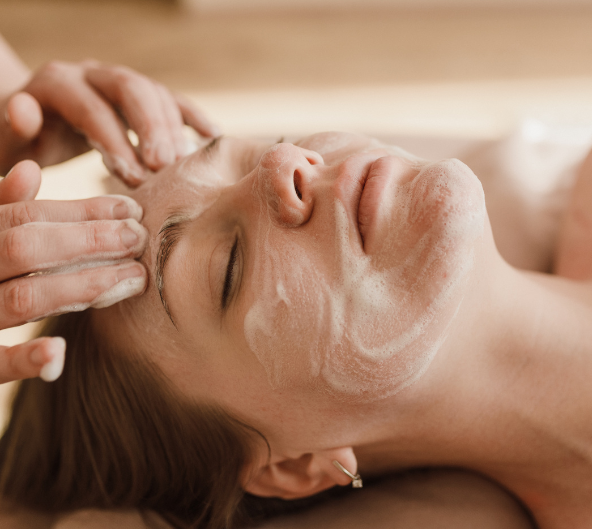 Personne recevant un soin du visage, les mains appliquant une crème blanche sur le front et le visage.