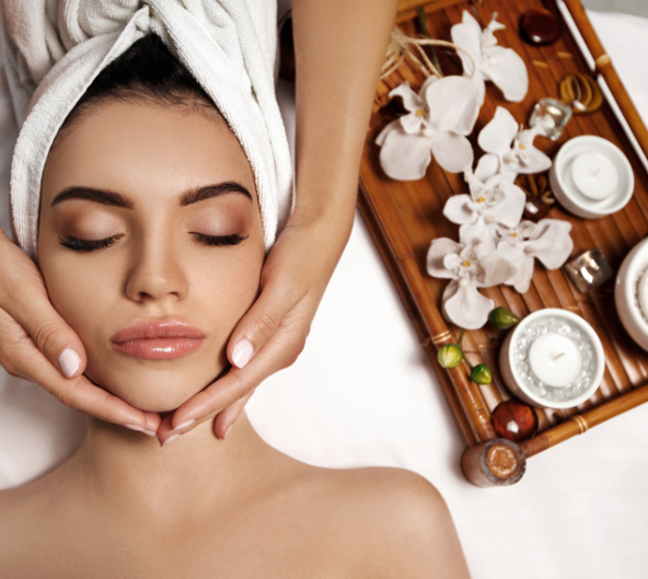 Une femme reçoit un massage du visage dans un spa ; ses mains touchent doucement son visage, les yeux fermés.