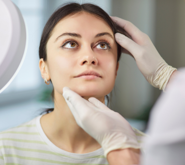 Femme dont le visage est examiné par des mains gantées ; contexte clinique.