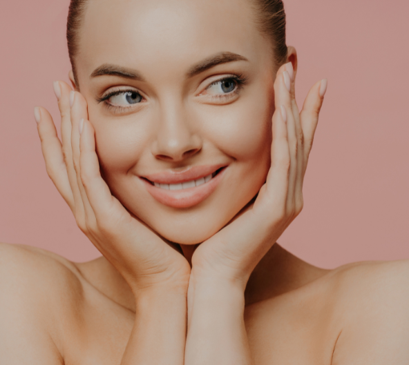 Femme souriante, touchant son visage avec les deux mains ; fond rose.