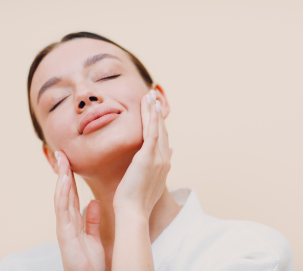 Femme aux yeux fermés, se touchant les joues. Vêtue d'une robe blanche, sur fond neutre.