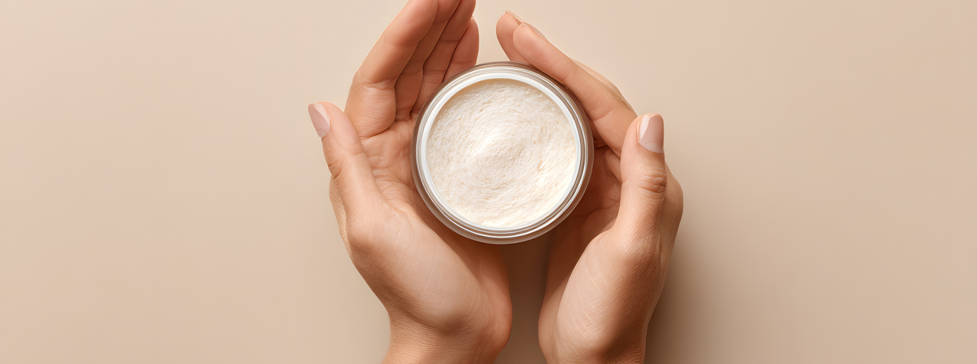 Mains tenant un pot de crème blanche sur un fond neutre.