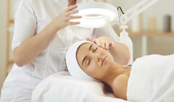 Une femme reçoit un soin du visage sous une lumière vive.