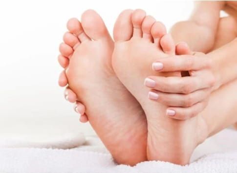 Les pieds de la personne reposent sur une serviette blanche, les mains touchant la plante des pieds.
