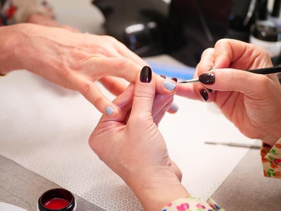 Manucure appliquant du vernis à ongles sur la main d'une cliente dans un salon.