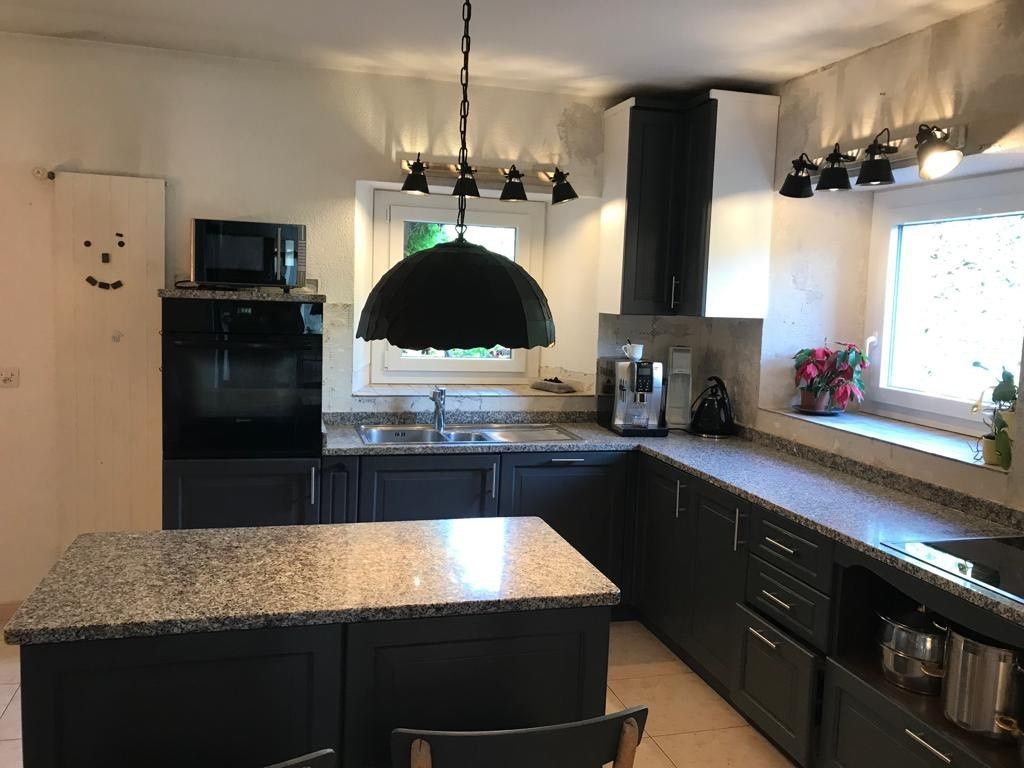 Une cuisine avec un grand îlot et une lampe noire suspendue au plafond après rénovation