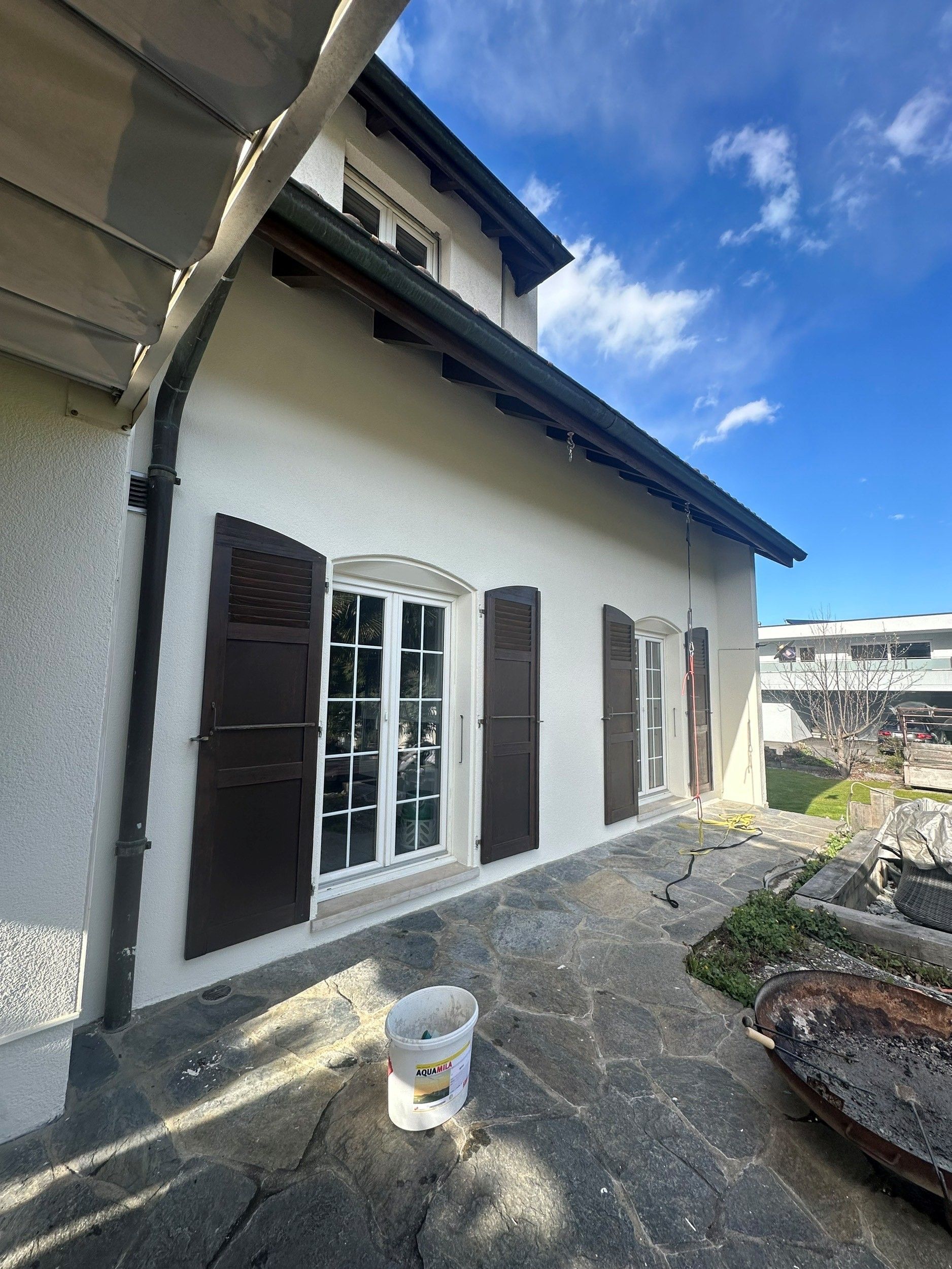 Une maison blanche avec des volets marron et un pot de peinture devant, après rénovation