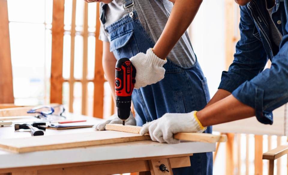Ein Mann bohrt mit einer Bohrmaschine ein Loch in ein Stück Holz.