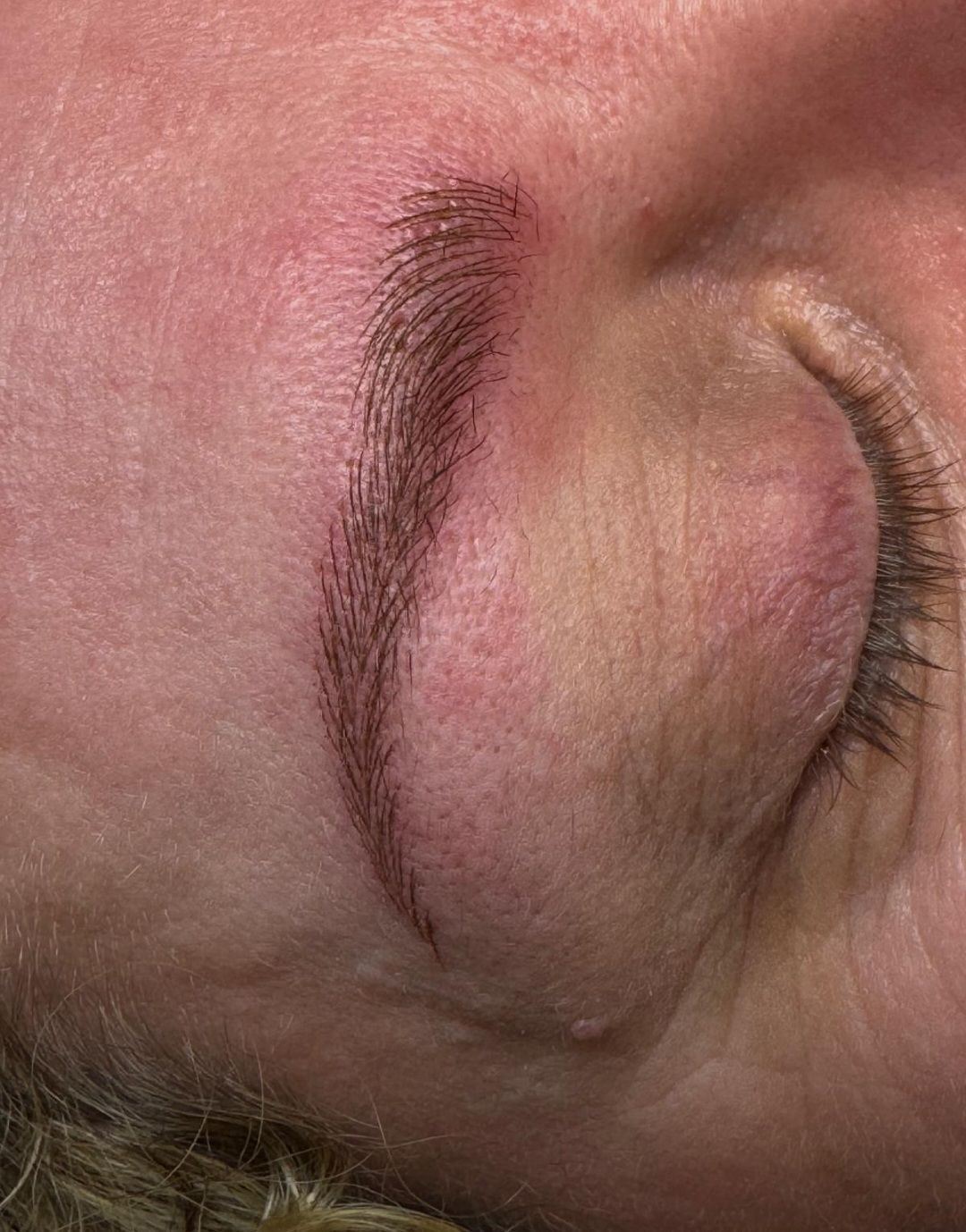 Nahaufnahme eines geschlossenen Auges mit geschwungener Augenbraue und sichtbarer rosa Haut.