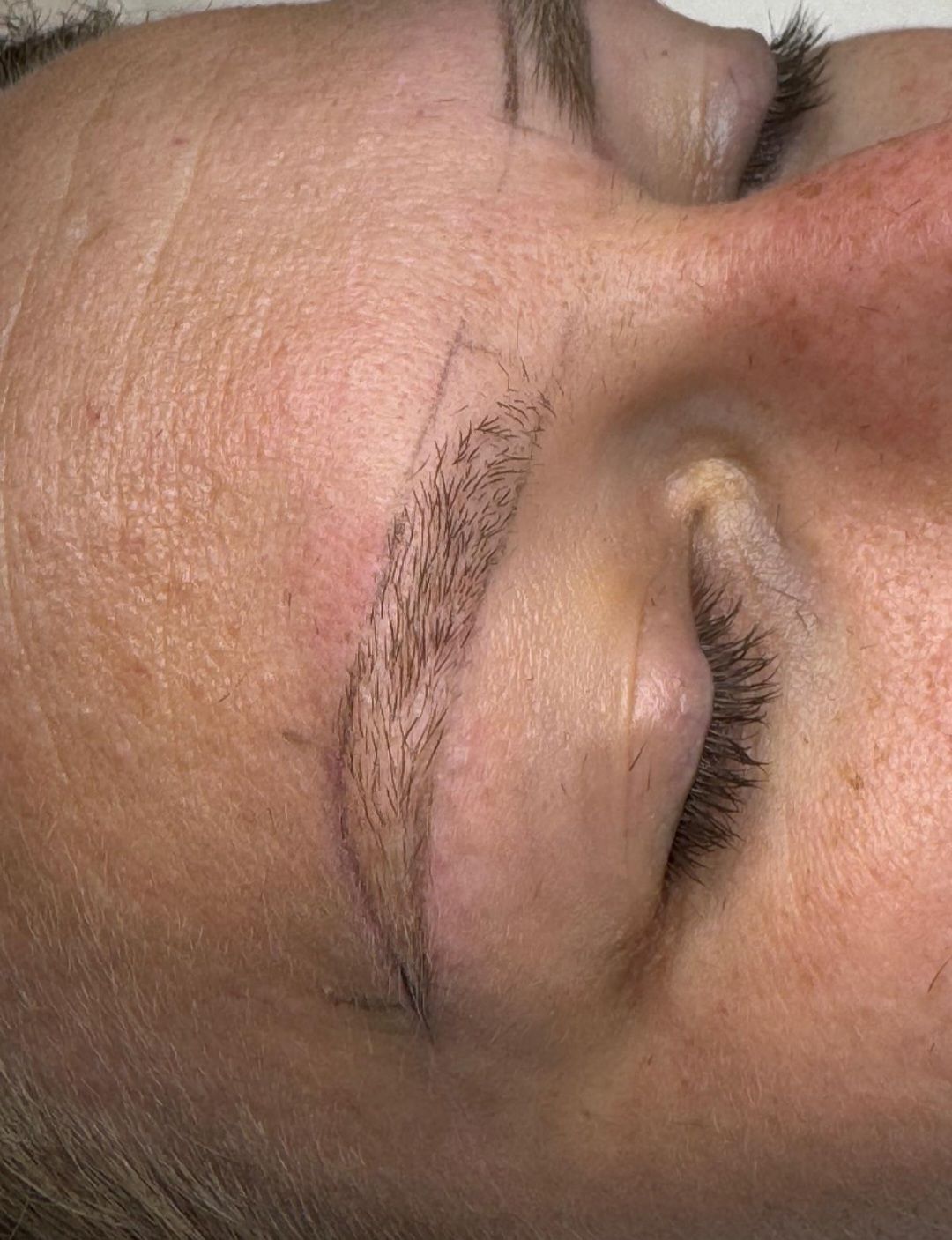 Nahaufnahme eines geschlossenen Auges mit Augenbrauen-Make-up auf der Haut, die ein kosmetisches Augenbrauendesign zeigt.