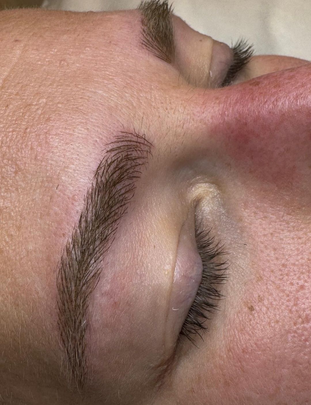 Nahaufnahme eines geschlossenen Auges mit ordentlich geformten Augenbrauen und langen Wimpern.