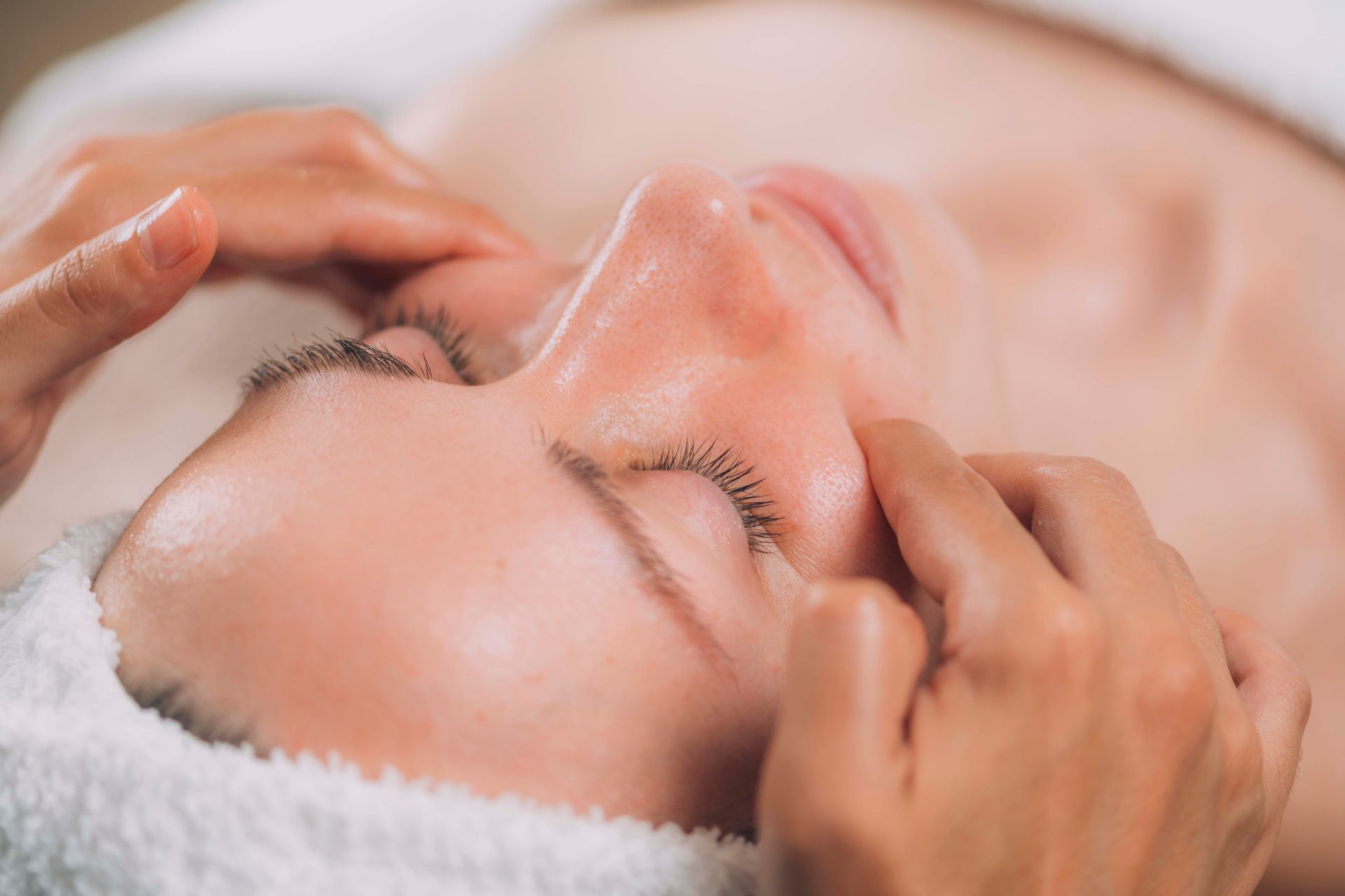 Nahaufnahme einer Gesichtsmassage, bei der die Hände sanft Schläfen und Stirn auf einer Spa-Liege drücken.