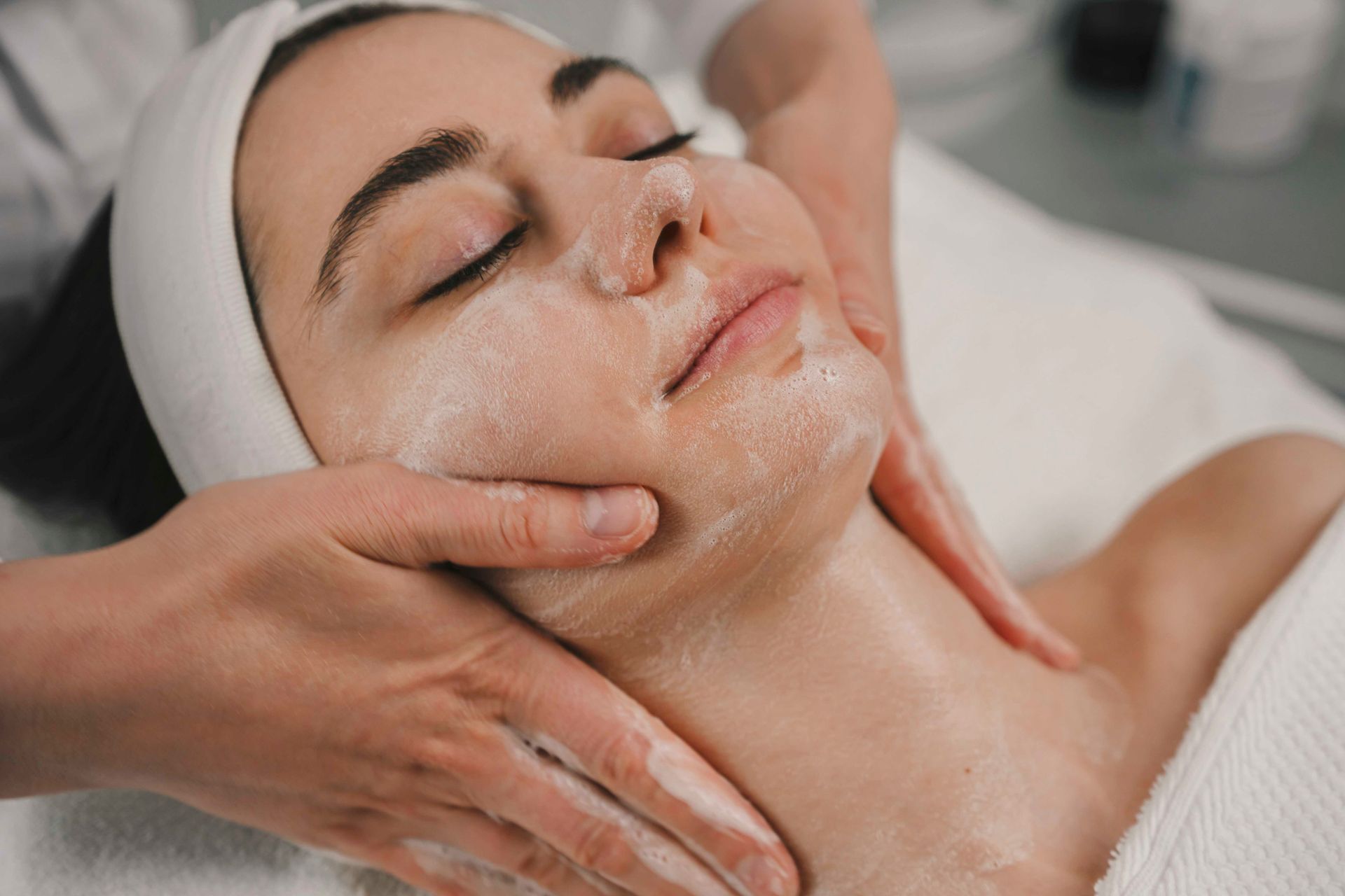 Gesichtsbehandlung im Spa, bei der eine Frau liegt, während Hände ihr Gesicht und ihren Hals massieren.