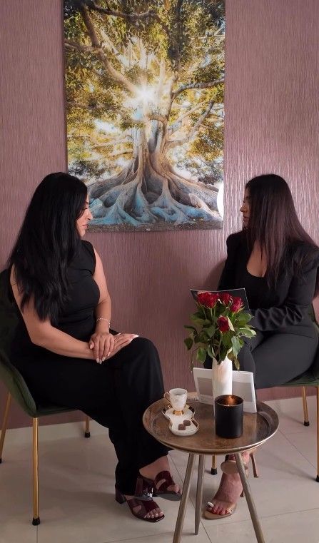 Zwei Frauen sitzen an einem kleinen Tisch und betrachten ein Baum-Kunstwerk in einem sanft beleuchteten Raum
