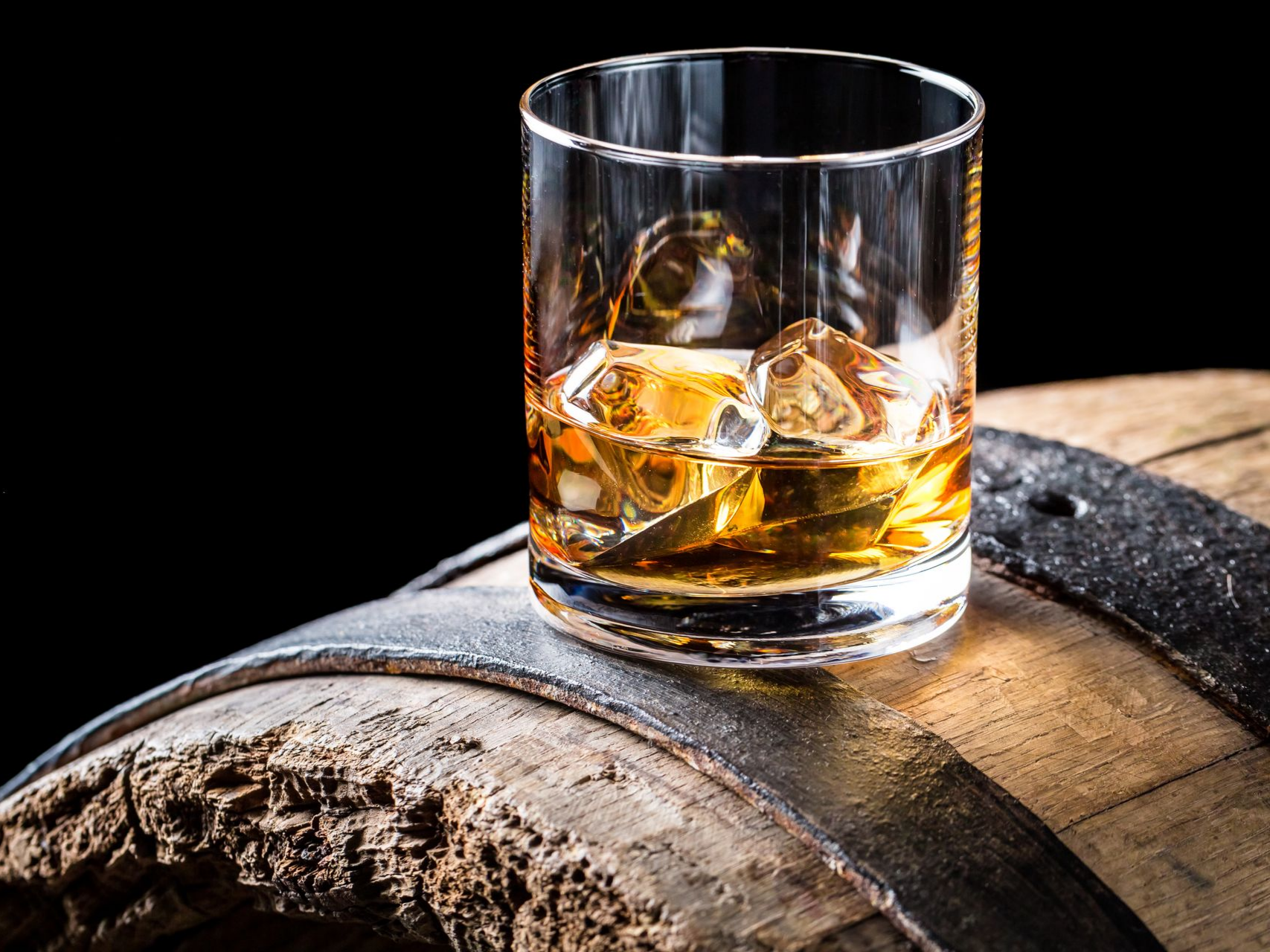 Un verre de liquide ambré avec de la glace sur un tonneau en bois.