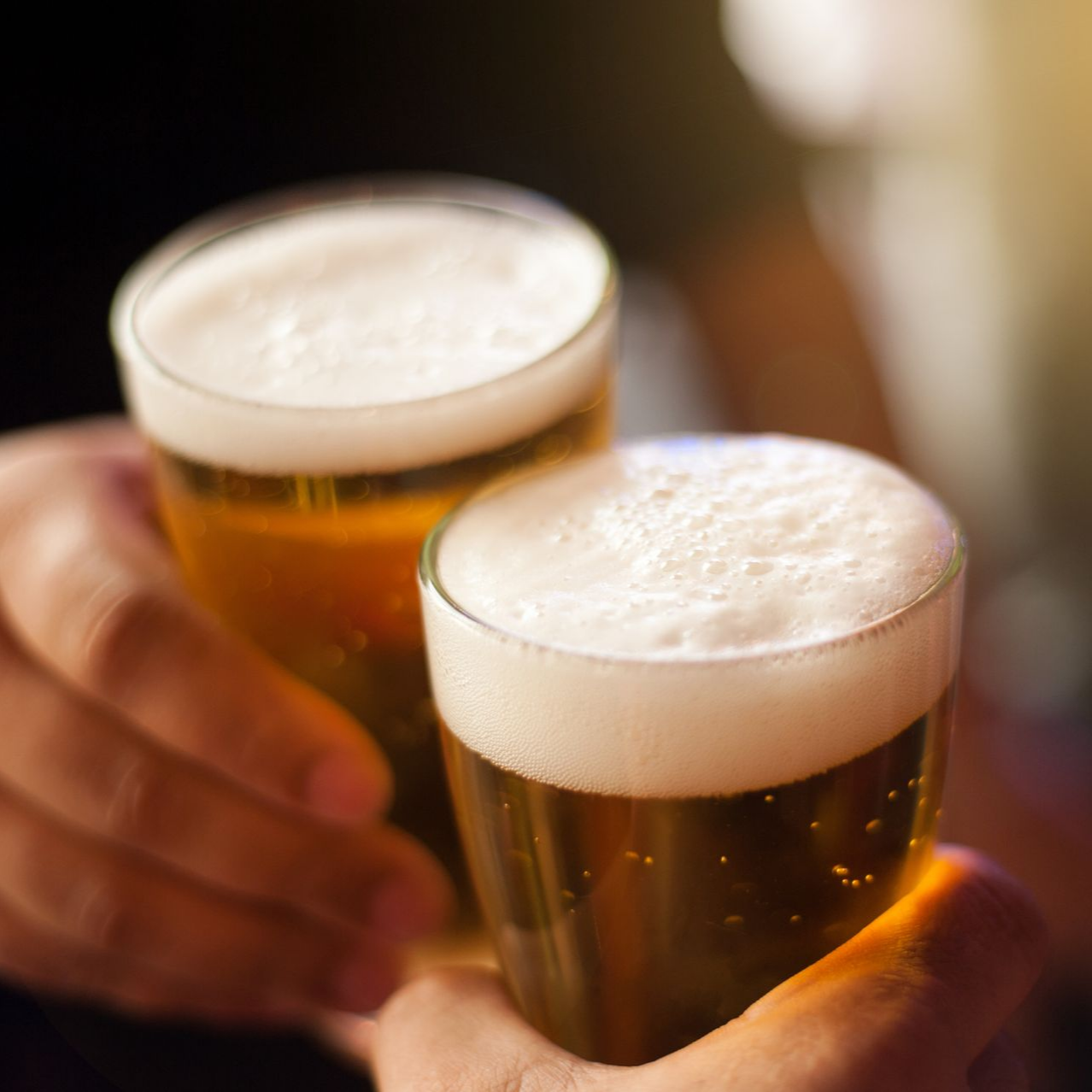Deux verres de bière s'entrechoquent, tenus à bout de bras.