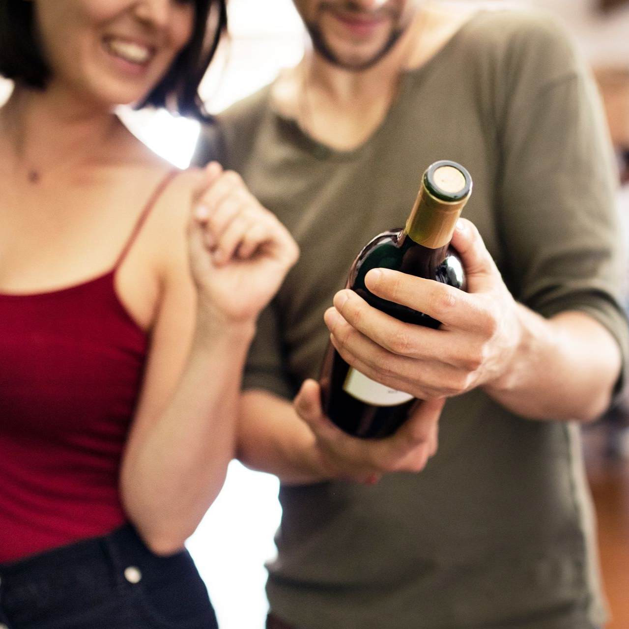 Un homme tient une bouteille de vin, une femme regarde en souriant.